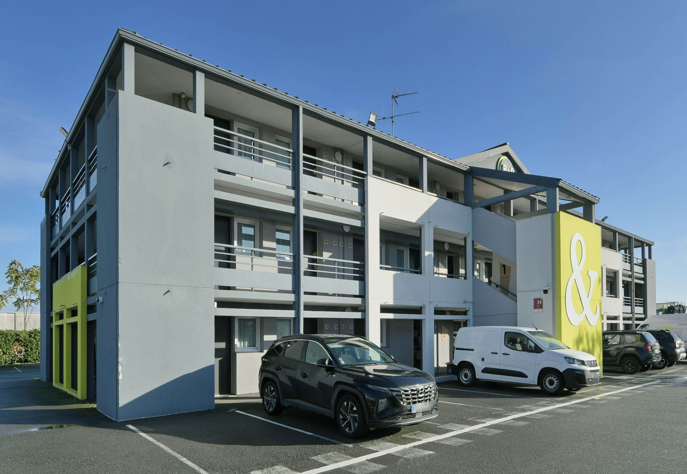 Un edificio a più piani con un'area di parcheggio, un furgone bianco e un'auto nera parcheggiati davanti.