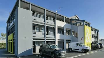 Un edificio a più piani con un'area di parcheggio, un furgone bianco e un'auto nera parcheggiati davanti.