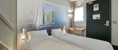 Habitación de hotel con dos camas, un escritorio, una silla, un ventanal con vistas y una puerta con un calendario.