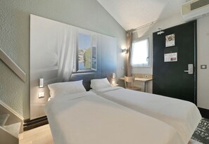 Ein Hotelzimmer mit zwei Betten, einem Schreibtisch, einem Stuhl, einem Fenster mit Aussicht und einer Tür, an der ein Kalender hängt.