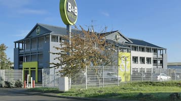 A B&B hotel with a modern design, featuring a prominent sign, a gated entrance, and a parking area.