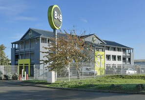 A B&B hotel with a modern design, featuring a prominent sign, a gated entrance, and a parking area. - B&B Hotel Le Mans Sud (Arnage)