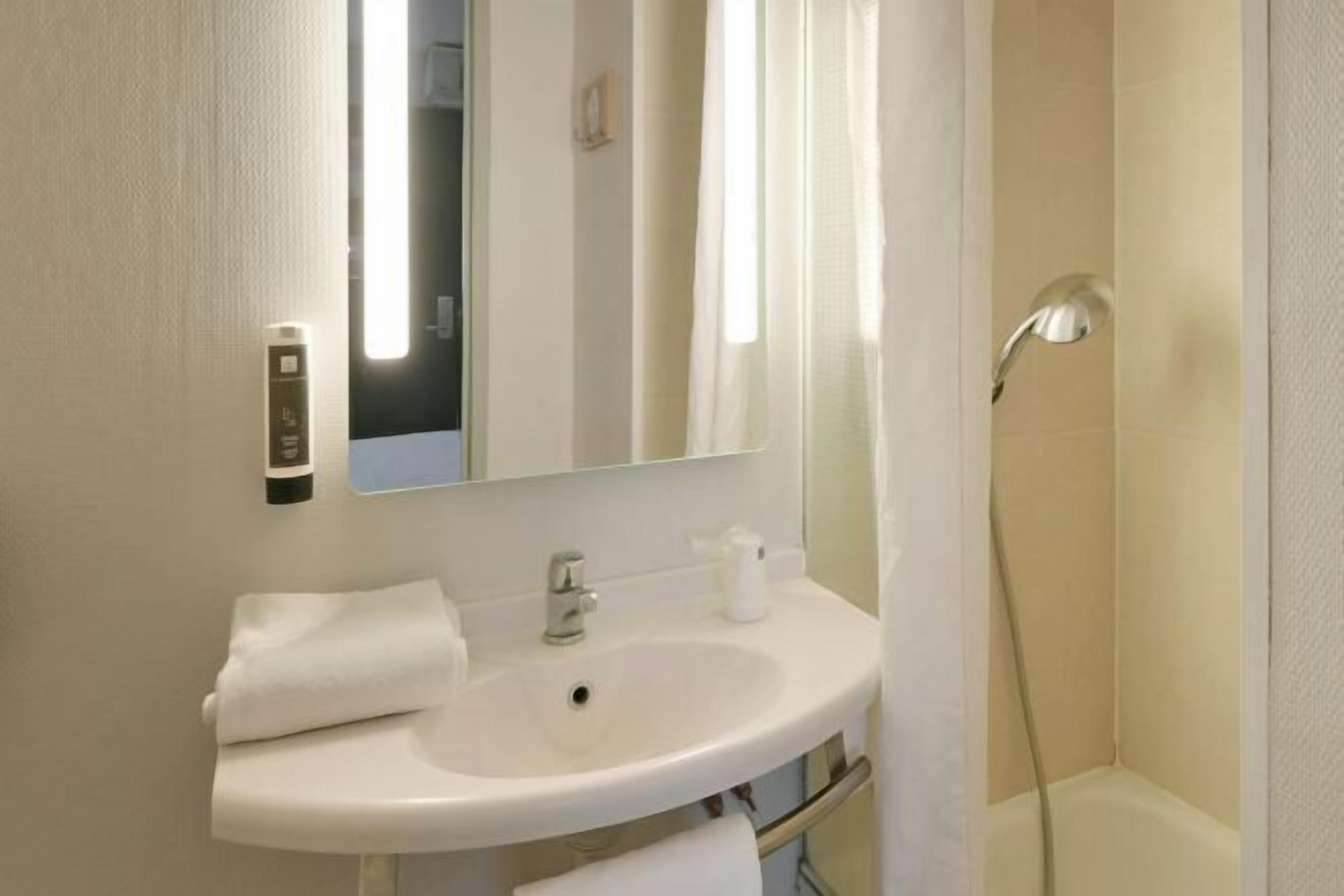 Un baño con un lavamanos blanco, un espejo, una toalla y una ducha.
