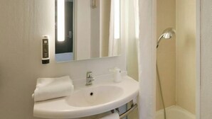 Ein Badezimmer mit einem weißen Waschbecken, einem Spiegel, einem Handtuch und einer Dusche.