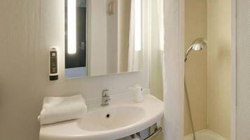 Un baño con un lavamanos blanco, un espejo, una toalla y una ducha.