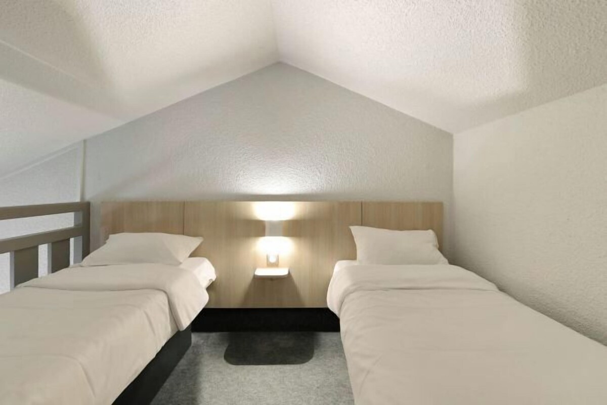A room with two beds, a wooden headboard, a nightstand with a lamp, and a small rug.