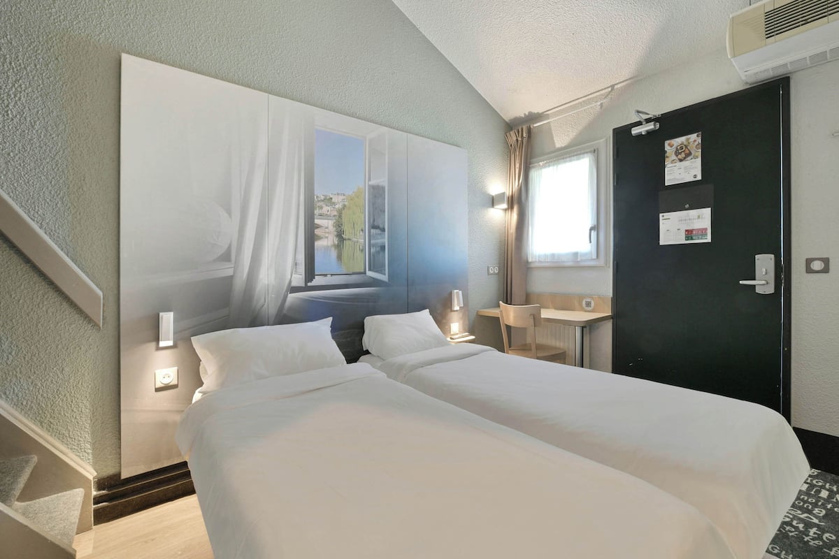 Hotelkamer met twee bedden, een bureau, een stoel, een raam met uitzicht en een deur met een agenda.