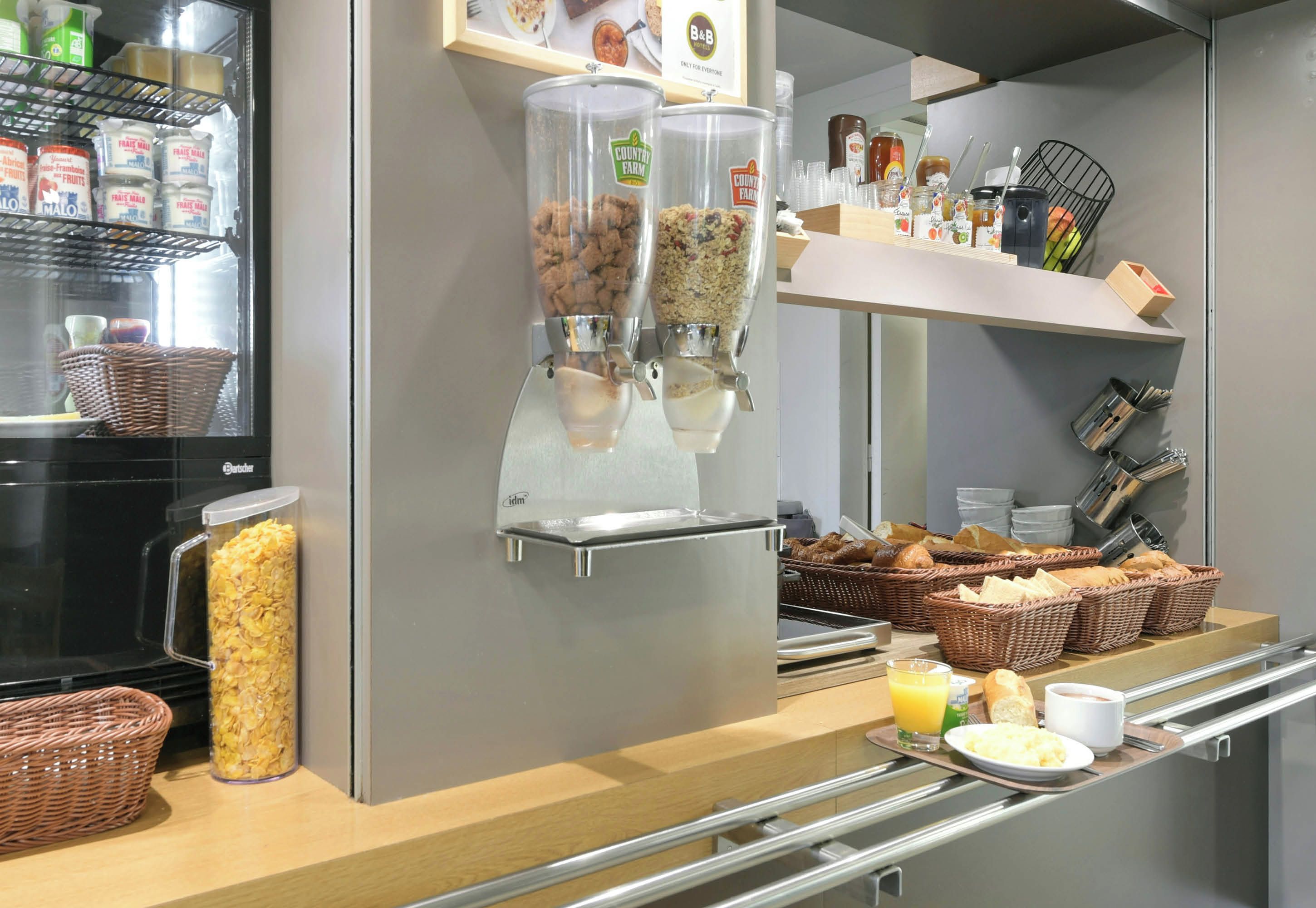 A breakfast buffet with cereal dispensers, baskets of bread, and a variety of condiments.