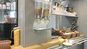 A breakfast buffet with cereal dispensers, baskets of bread, and a variety of condiments.