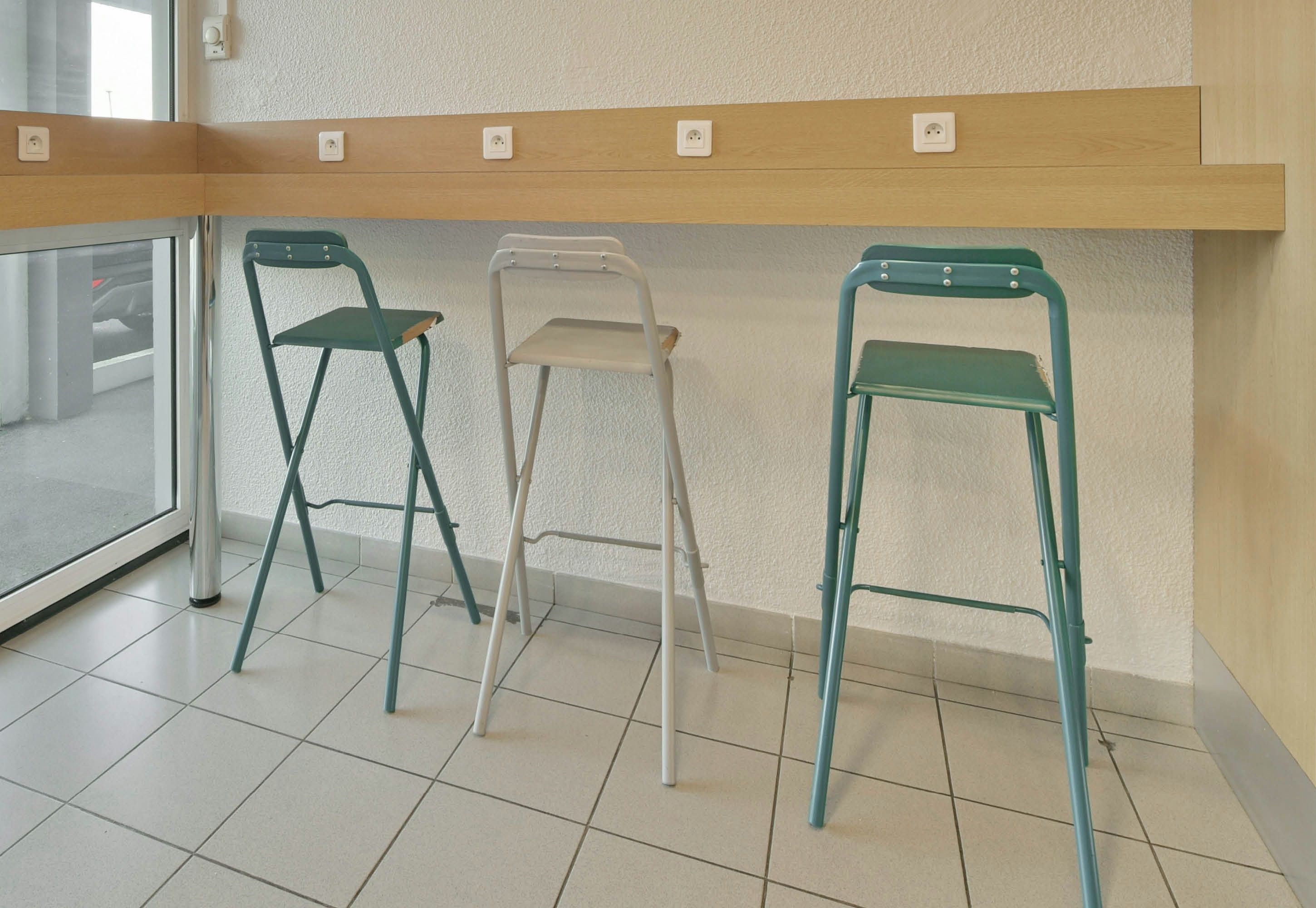 Three foldable chairs, a wooden shelf with electrical outlets, and a tiled floor.
