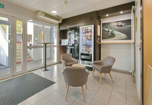 A reception area with a seating arrangement, a vending machine, and a wall-mounted artwork. - B&B Hotel Le Mans Sud (Arnage)
