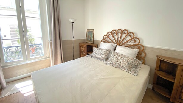Une chambre à coucher avec un lit, une table de chevet, une lampe sur pied et une fenêtre avec des rideaux.