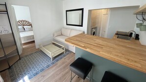Un espace de vie compact comprenant un coin cuisine, un canapé, une table à manger en bois et un petit coin bar.