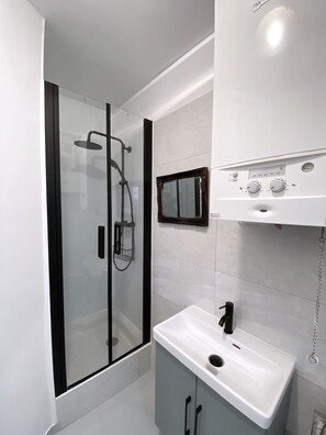 Un baño moderno con cabina de ducha de vidrio, un lavabo blanco y un espejo pequeño.