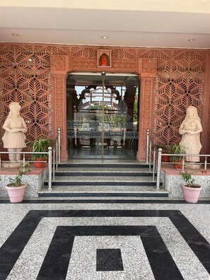 A hotel entrance with a decorative facade, a glass door, and steps leading up to it. - Seth Murlidhar Mansinghka Seva Sadan (Mathura)