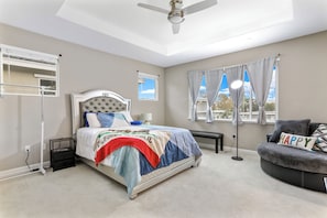 Ein Schlafzimmer mit Bett, einer Bank, einem Deckenventilator, einem Fenster mit Vorhängen und einem Nachttisch.
