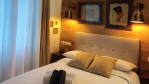 A hotel room with a wooden headboard, a bed with white linens, two pillows, a nightstand, a lamp, and wall-mounted artwork. - STUDIOS OR PRIVATE ROOMS (Barcelona)