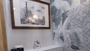 A bathroom with a framed black and white cityscape picture, a white shelf with a black object, a white toilet paper holder, and patterned tiles. - STUDIOS OR PRIVATE ROOMS (Barcelona)