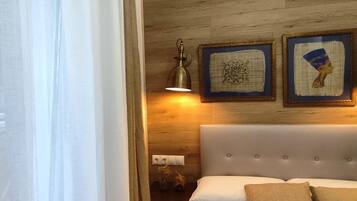 Un dormitorio con una cama, cabecera, lámpara de pared y dos cuadros enmarcados.