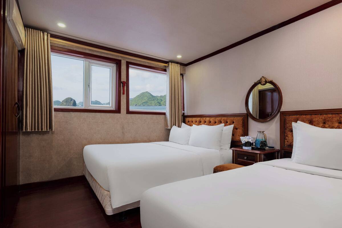 A hotel room with two beds, a wooden headboard, a nightstand, a mirror, and a window with curtains.