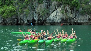 Un gruppo di persone che pagaia in kayak verdi su un fiume, con ripidi pendii rocciosi sullo sfondo.
