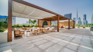 An outdoor seating area with a view of a city skyline, including a prominent skyscraper. - Charming 1BR w Balcony in Business Bay (Dubai)