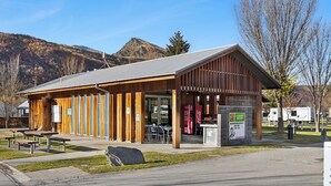 A wooden building with a sloped roof, outdoor seating, and a Coca-Cola vending machine. - Hampshire Holiday Parks - Arrowtown (Arrowtown)