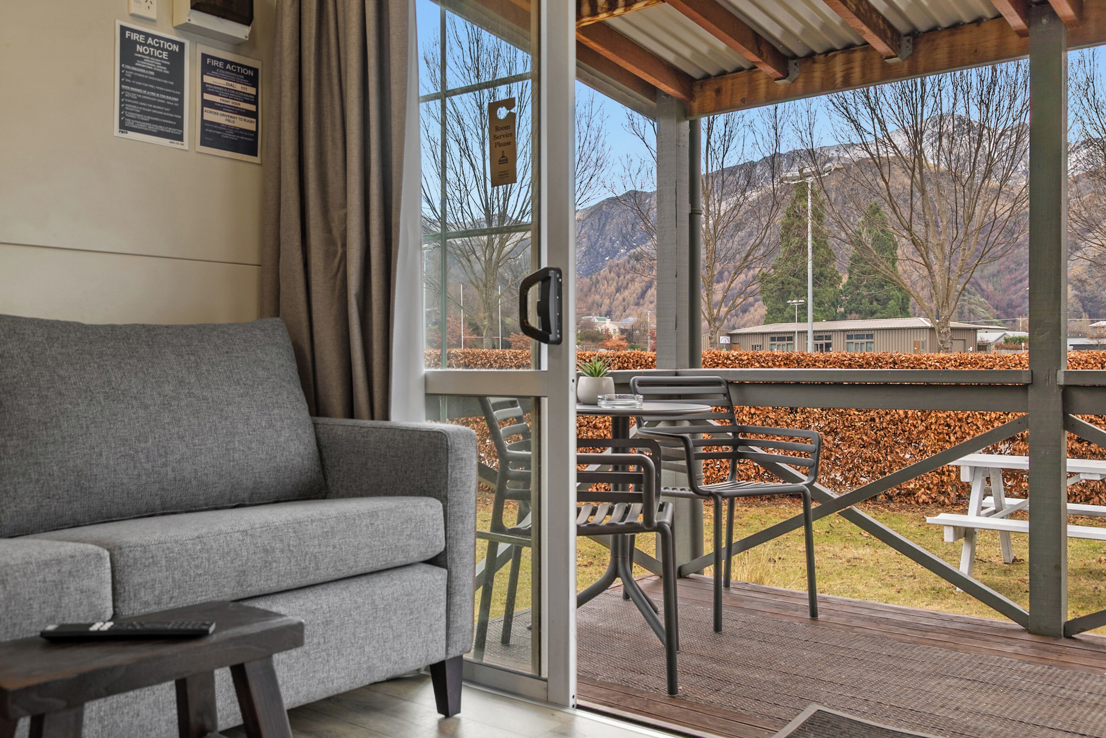 A room with a grey sofa, a small table, and a window overlooking a mountainous landscape.