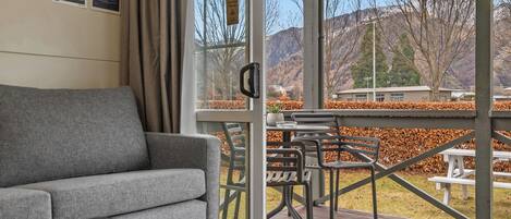 A room with a grey sofa, a small table, and a window overlooking a mountainous landscape.