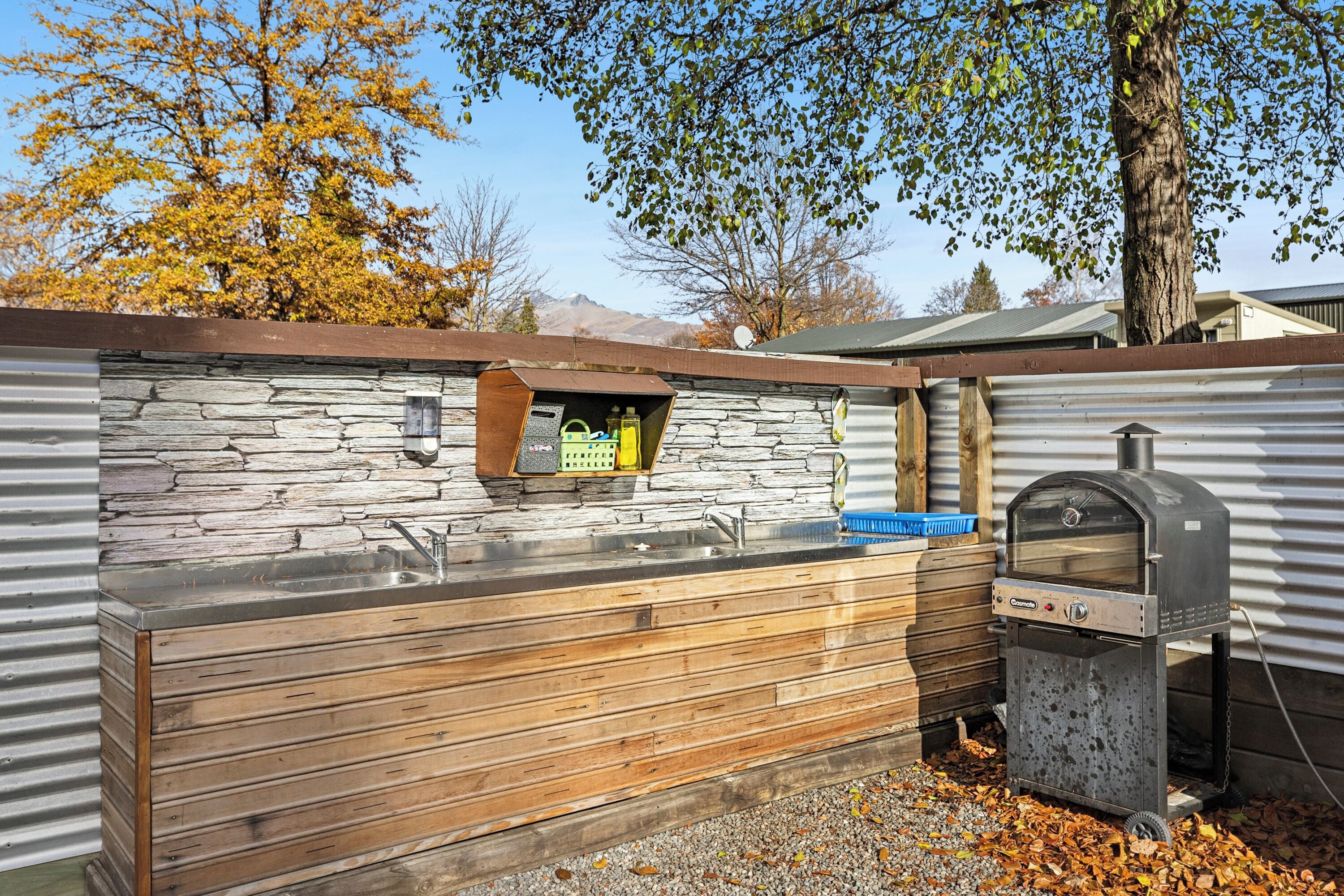 A stone and wood outdoor kitchen with a built-in sink and a pizza oven.