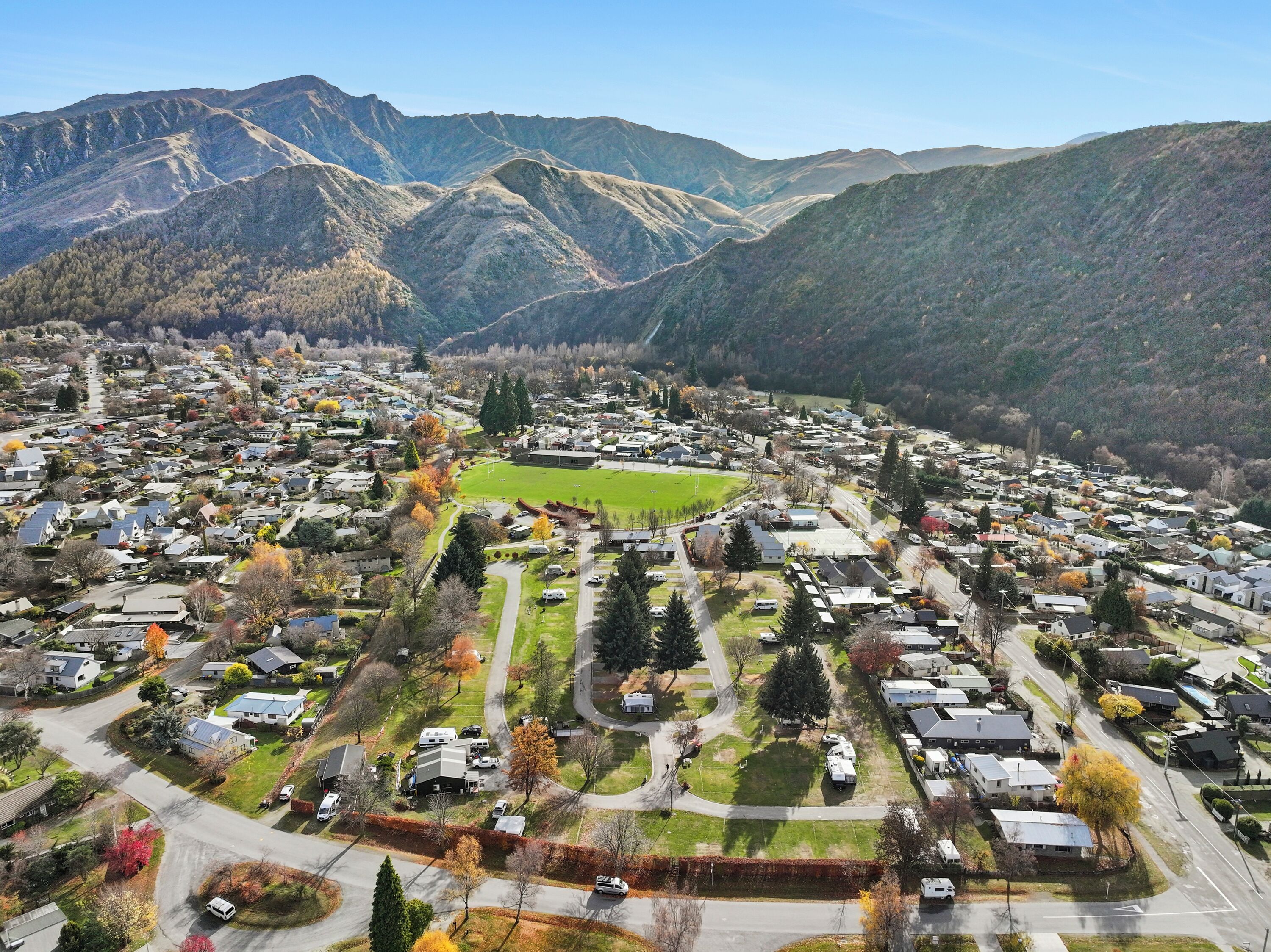 A residential area with houses, a green field, and mountains in the background.