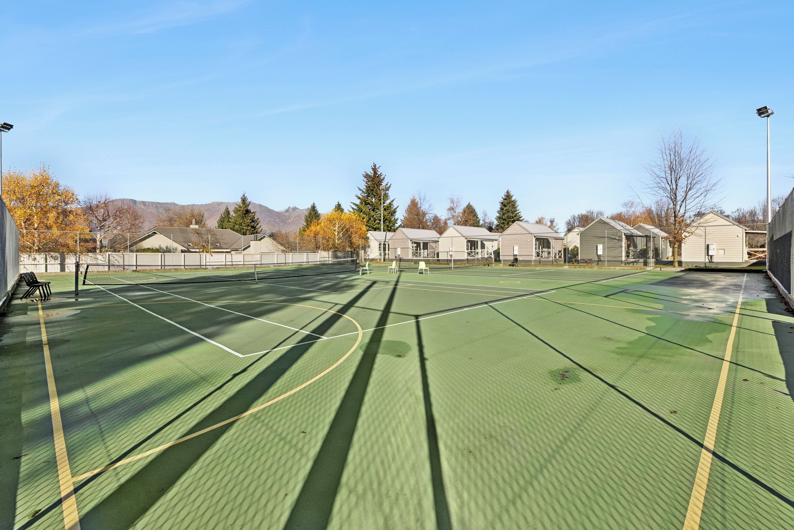Ein Tennisplatz im Freien mit Netz, umgeben von Gebäuden und Bäumen.