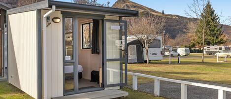 A portable restroom with a door, a small step leading up to it, and a view of the surrounding area including other portable structures and a mountain in the background.
