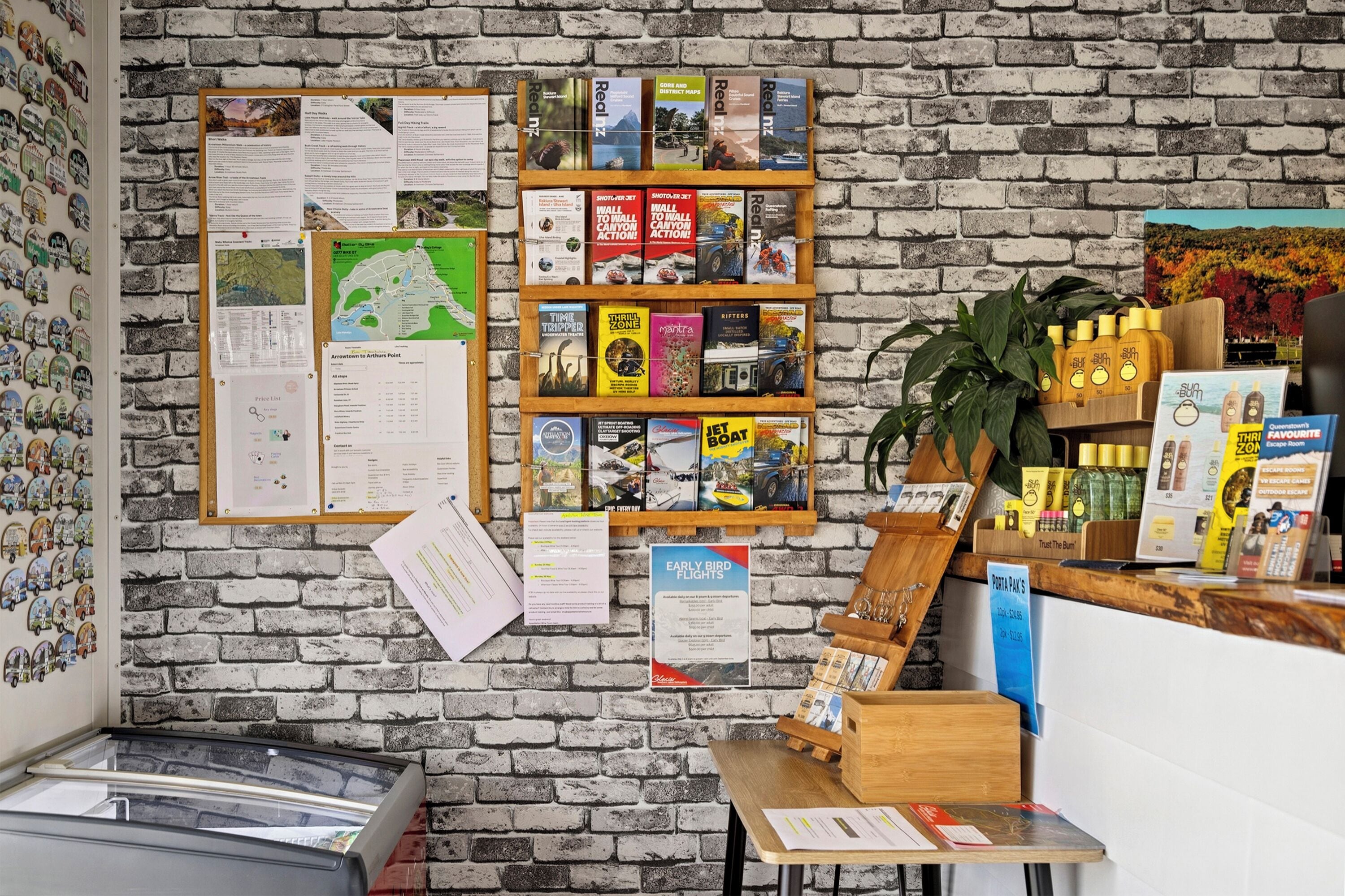 Una librería con un fondo de pared de ladrillo, varios libros de viajes y aventuras, y una pequeña planta en el mostrador.