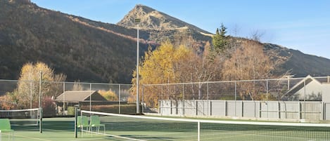 A tennis court with a net, surrounded by a fence, and a mountain in the background.