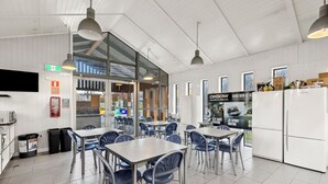 A modern dining area with tables and chairs, a kitchen area with a refrigerator, and a large window providing natural light. - Hampshire Holiday Parks - Arrowtown (Arrowtown)