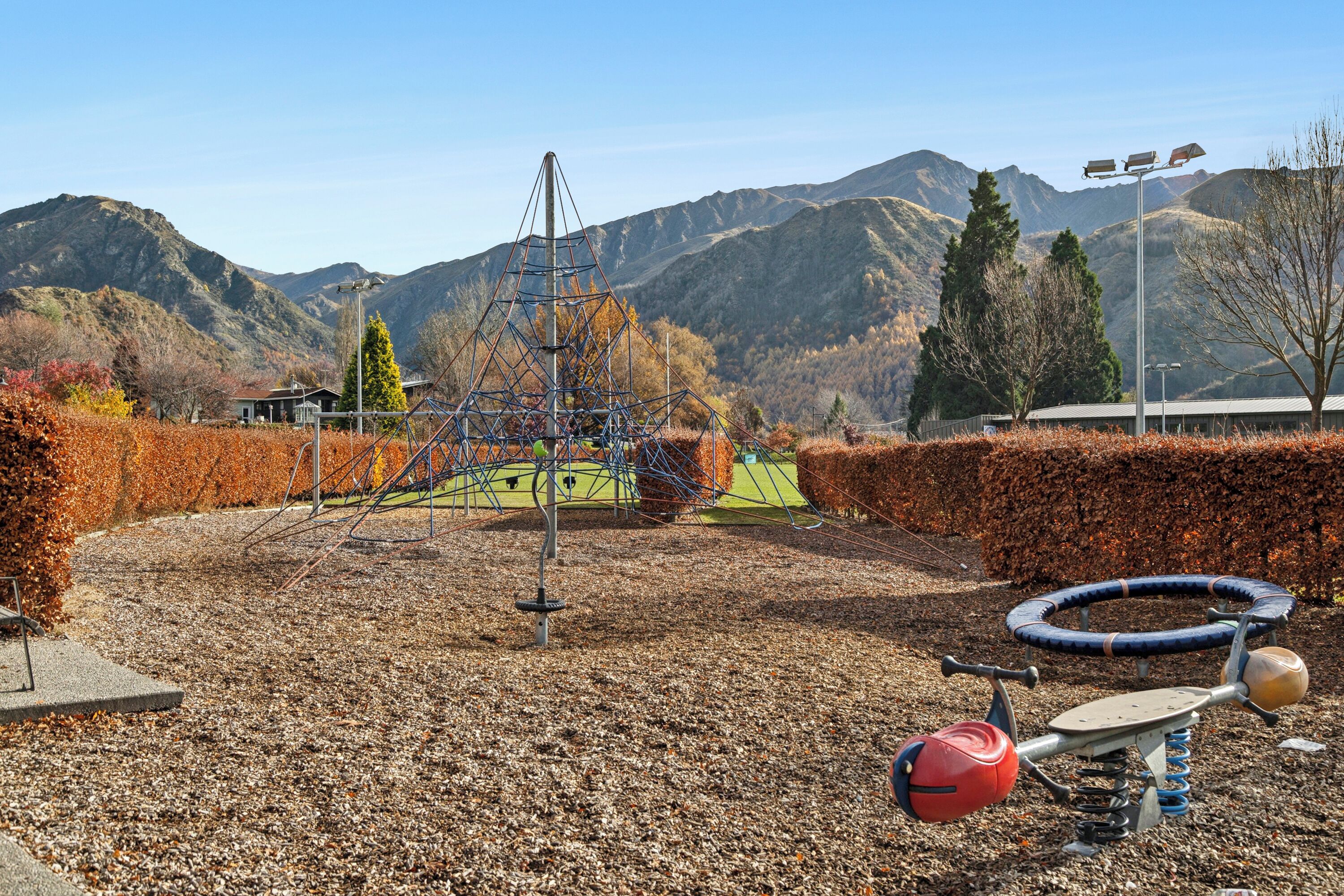 A playground with swings and a climbing structure, surrounded by autumn foliage and mountains.