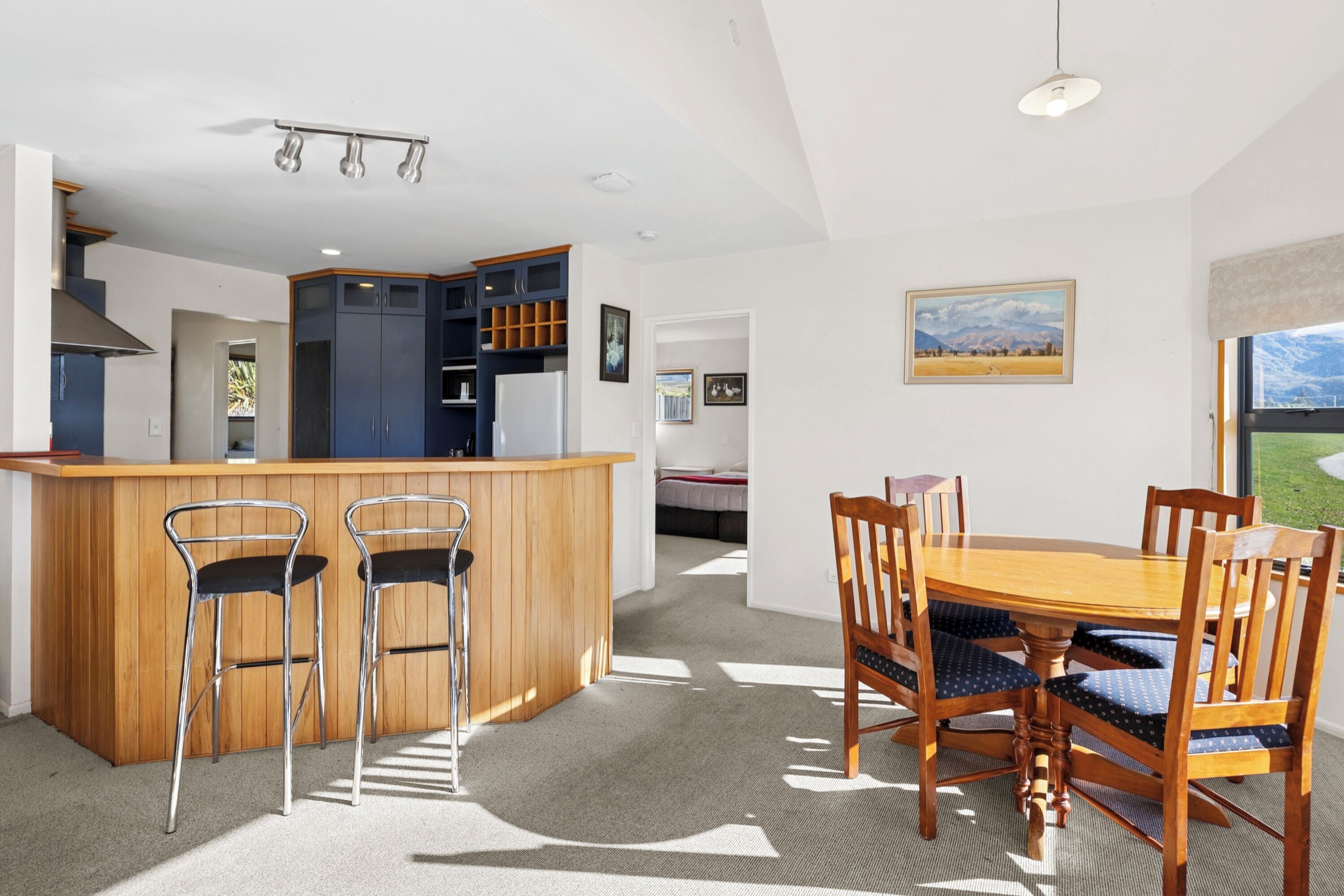 A modern kitchen with a wooden island, bar stools, and a dining table with chairs.