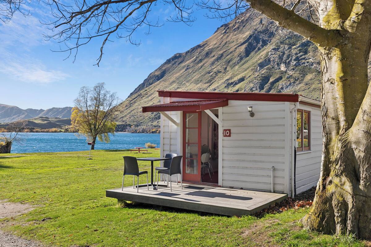 Une petite cabane blanche avec un toit rouge, une porte portant le numéro « 10 », et une table avec des chaises à l’extérieur.