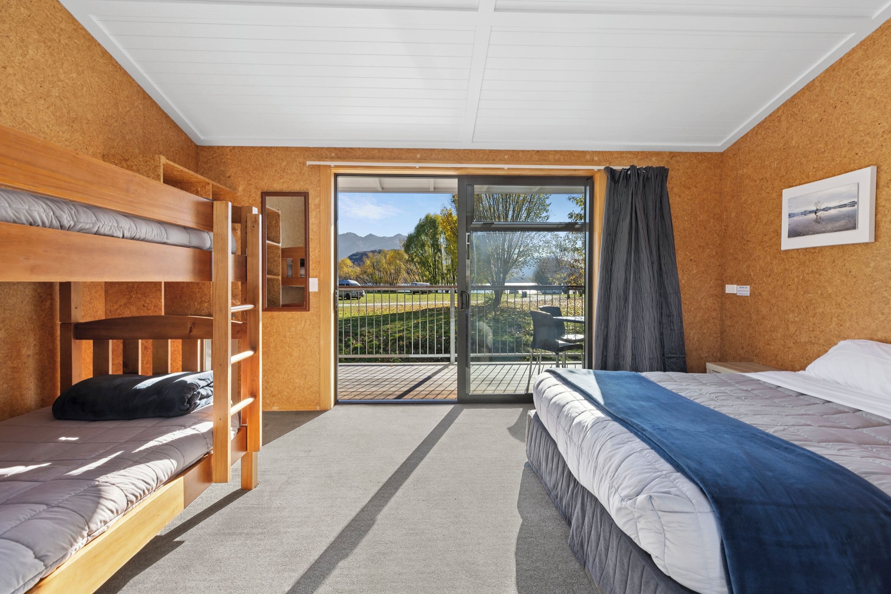 A room with bunk beds, a balcony with a view of mountains and trees, and a large window with curtains.