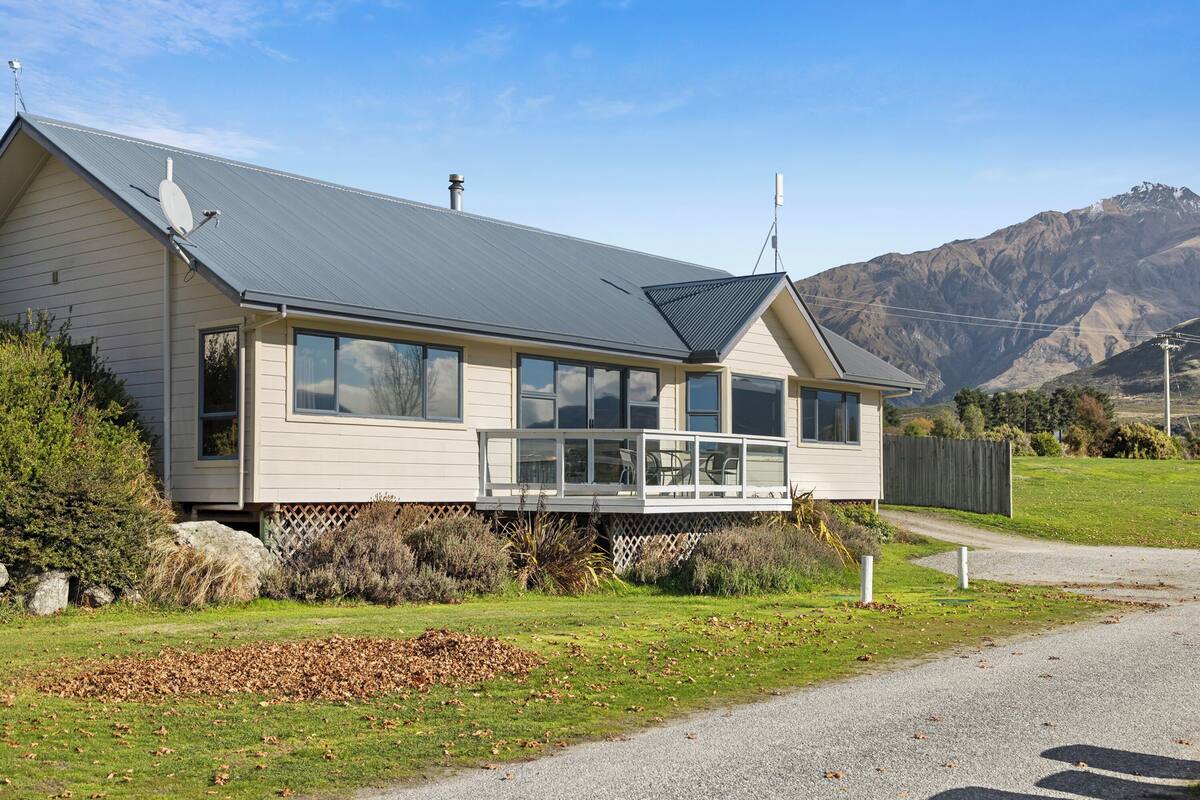 Une maison à deux étages avec un balcon, un toit en métal et une vue sur les montagnes en arrière-plan.