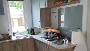 Una cuina compacta amb armaris de fusta, un fogó a gas i una finestra que deixa entrar llum natural.