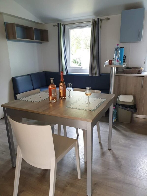 A dining area with a table, chairs, a bottle, and glasses. - Fully equipped premium mobile home in 4-star campsite le loyada (Talmont-Saint-Hilaire)