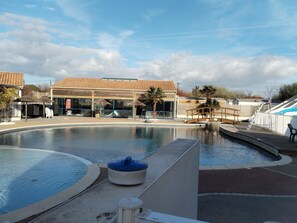 A swimming pool area with a water slide, umbrellas, and a building with a tiled roof. - Fully equipped premium mobile home in 4-star campsite le loyada (Talmont-Saint-Hilaire)