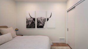 A bedroom with a bed, a nightstand, a lamp, and two wall-mounted pictures of a bull. - Creekside 2-bedroom cottage mid-valley (Hailey)