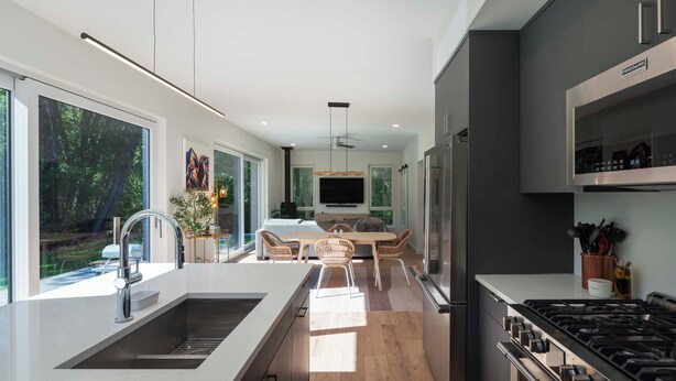 A modern kitchen with a central island, a dining area with a table and chairs, and a large window providing a view of the outdoors. - Creekside 2-bedroom cottage mid-valley (Hailey)