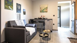 Una sala de estar moderna con un sofá gris, una mesita redonda y una zona de cocina con un taburete de bar.