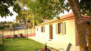 Un patio con una mesa lista para dos, una silla y un pequeño pabellón al fondo.