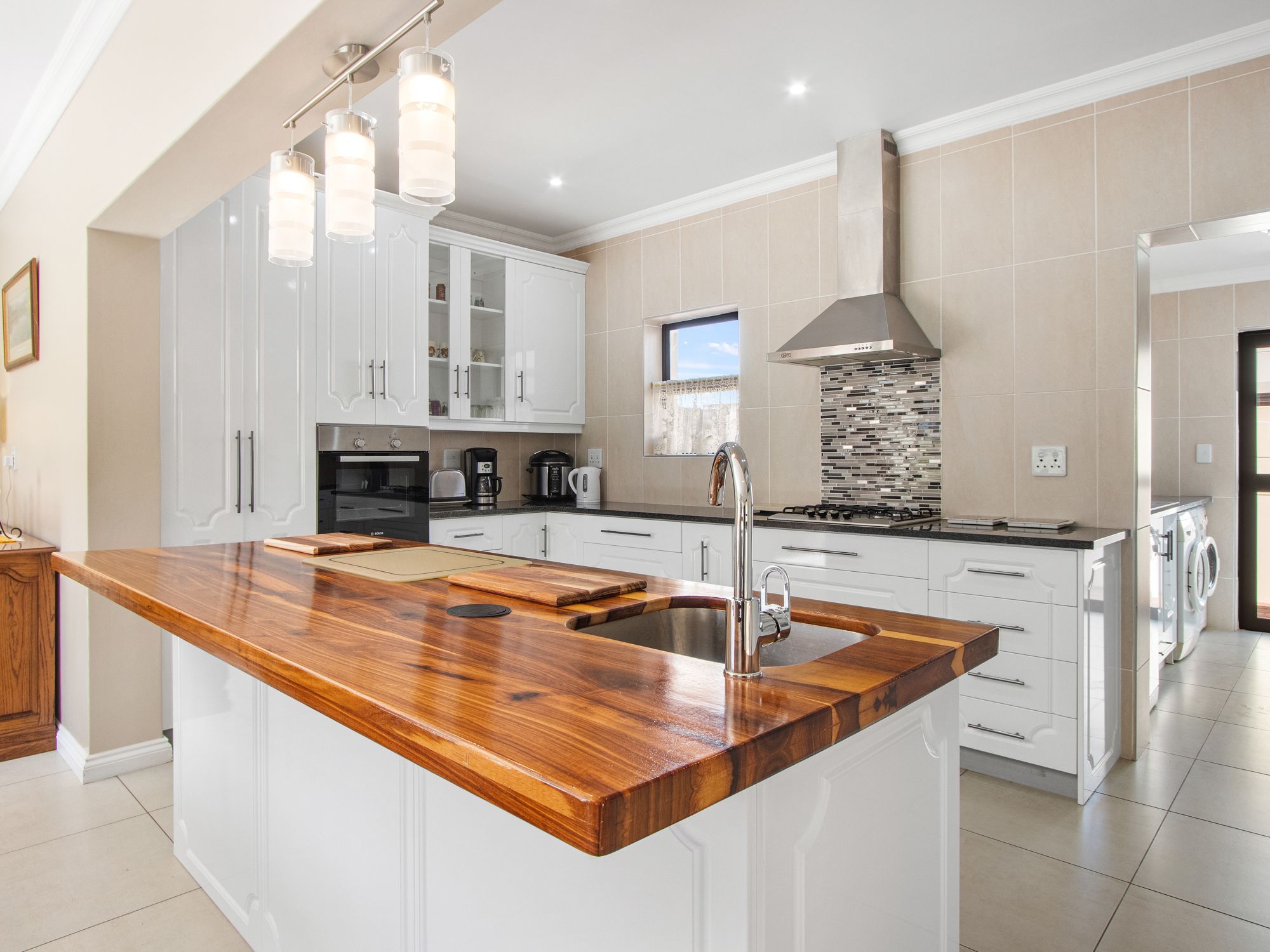 A modern kitchen with white cabinets, a wooden island, stainless steel appliances, and a large window.
