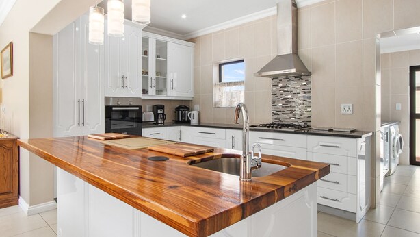 Een moderne keuken met witte kasten, een houten eiland, roestvrijstalen apparatuur en een groot raam.